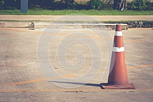 Old orange traffic cone standing on concrete floor in front of empty parking lot for reservation.