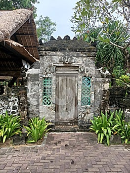 old ornate doorway with frangipani trees and thatched roof houses