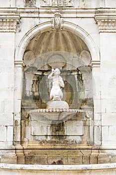 Old ornate water fountain set in a white stone wall with a statue and shell ornamentation
