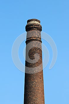 An old and out-of-use brick industrial plant chimney against a blue clear sky