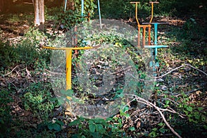 Old outdoor exercise equipment so worn out and covered in trees in outdoor exercise park. Old abandoned gym equipment on sports