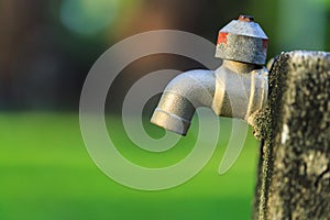 Old outdoor faucet without water in garden on green blur background