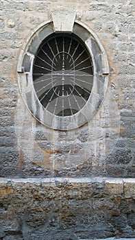 Old oval window with a metal grille set in a stone wall
