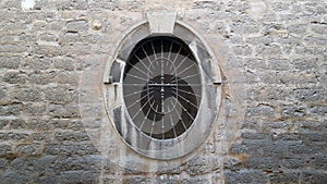 Old oval window with a metal grille set in a stone wall