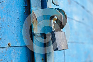 old padlock on a blue metal door with wooden planks cracked paint and rust