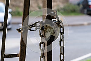 An old padlock on a chain of locked iron gates against the background of blurred cars on the street