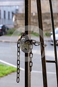 An old padlock on a chain of locked iron gates against the background of blurred cars on the street