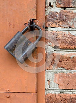 Old padlock on metal door. Red brick wall