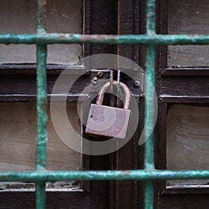 Old padlock on the old wooden door behind a grid