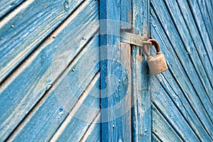 Old padlock on a weathered retro blue wooden door. Textured background.