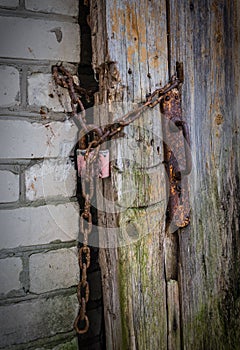 Old padlock on a wooden door. Wooden door locked with padlock close-up, focus on lock. Rusty padlock with chain on the door