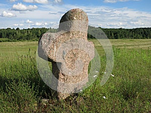 An old pagan cemetery in Belarus. Stone pink cross made of granite. humanlike