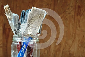 Old paint brushes on pressed wooden panel background
