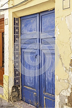 Old painted blue door of weathered wood and ceramic tiles on an old plaster wall in Spain