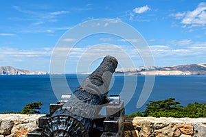 Old painted cannon pointing on a calm waveless sea under a cloudy sky