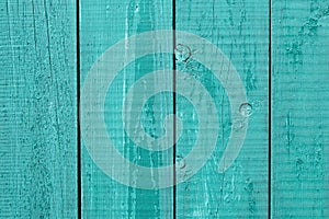 Old painted turquoise wooden fence. Cracked wood timber, blue shabby planks, green flaky grunge background. Oak table. Rustic weat