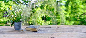 old paper book in black cover, family bible lie on wooden table in garden, beautiful blurred natural landscape in background with