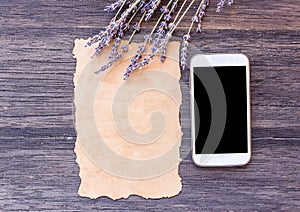 Old paper and smart phone with lavender flower on dark wooden ta