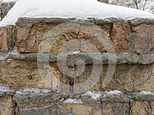 Old partly destroyed brick wall covered with hoarfrost and snow