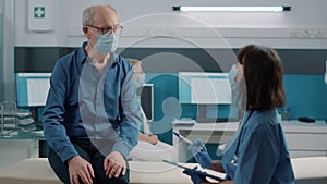 Old patient with face mask having conversation with female nurse