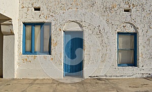 Old peeling paint wall with a blue door and two blue framed windows, vintage rustic background