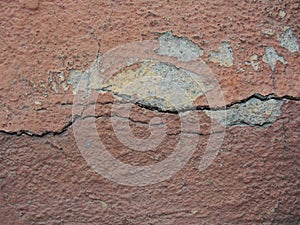 Old peeling red terracotta pink plaster on a cracked rough, scratched uneven concrete stone wall.