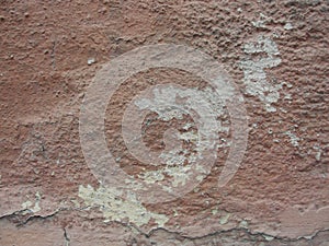 Old peeling red terracotta pink plaster on a cracked rough, scratched uneven concrete stone wall.