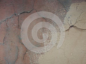 Old peeling red terracotta pink plaster on a cracked rough, scratched uneven concrete stone wall.