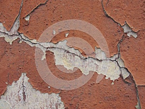 Old peeling red terracotta pink plaster on a cracked rough, scratched uneven concrete stone wall.