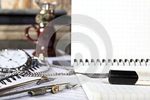 The old penholder for the pen and the retro compass lie on the open notebook. Sharpness on the tip of the pen. Close-up.