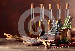Old pepper mill with cooking utensils, bottles of olive oil, spices and rosemary on a wooden table