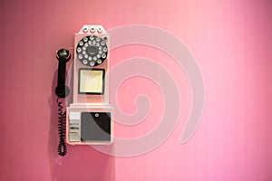 Old phone hanging on a pink wall