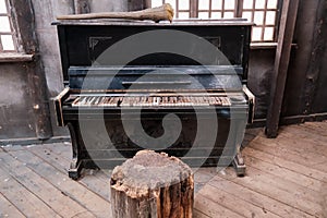 An old piano in a dirty room of an abandoned house. Black piano with white keys covered in dirt