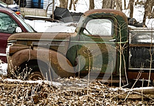 An old pickup truck sits abandoned in a yard as it rusts away.