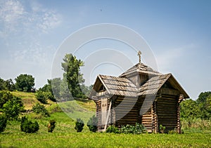 Old picturesque wooden village chapel and sunny summer meadow