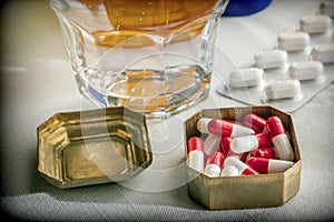 Old pillbox with capsules red and white next to a glass of water