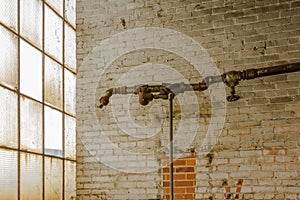 Old pipe running along painted brick wall next to frosted windows in an abandoned factory