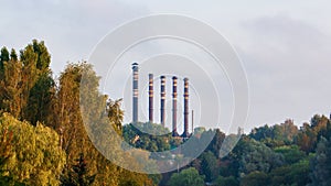 Old pipes of a thermal power plant against the background of the sky and trees in early autumn