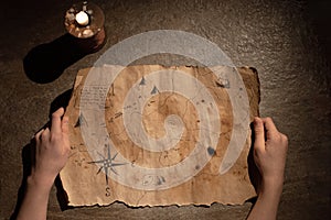 old pirate map drawn on aged paper in hands, candle on the table, treasure hunt and adventure search concept