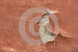 The old plaster on the orange wall is falling off in a big chunk