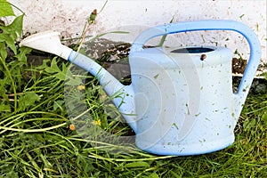 Old plastic blue garden watering can against a background of green grass.