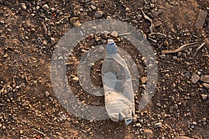 an old plastic bottle lies on the ground, yellow sand and stones on lifeless earth,