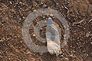 An old plastic bottle lies on the ground, yellow sand and stones on lifeless earth, a crumpled bottle thrown by people,