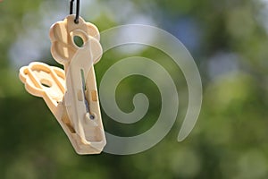 Old plastic clothpin hanging on blurred tree background