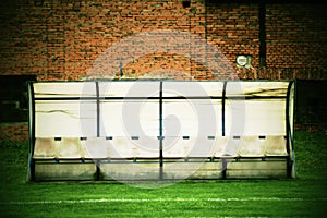 Old plastic seats on outdoor stadium players bench, chairs with worn paint below yellow roof.