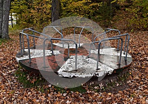 Old playground merry go round covered with fall leaves