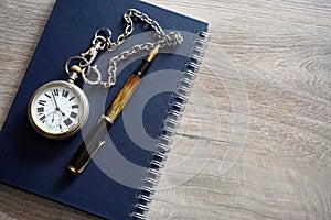 Old pocket watch with chain, fountain pen and note on a wooden surface
