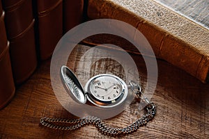 An old pocket watch with a chain lies on the table near vintage books