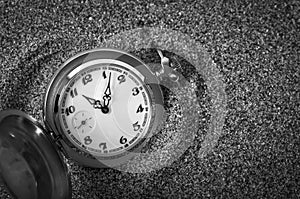 An old pocket watch lying in the sand.