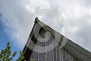 The old pointed roof of a village house with a singing bird sitting on it against a cloudy sky